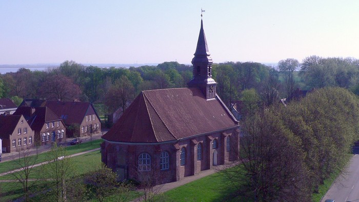 Kirche mit hohem Turm inmitten von Grünflächen und Häusern.
