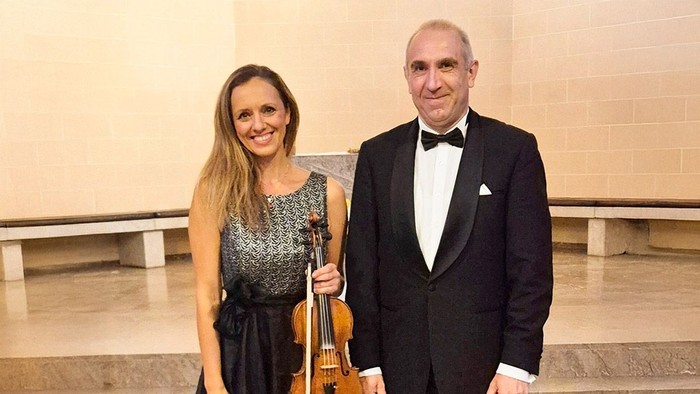 Ein Mann im Smoking und eine Frau in einem schwarzen Kleid mit Geige posieren auf einer Treppe