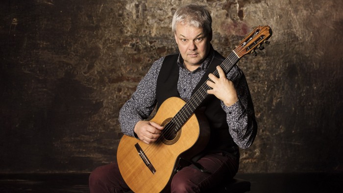 Ein Mann spielt eine Gitarre vor einer dunklen Wand.