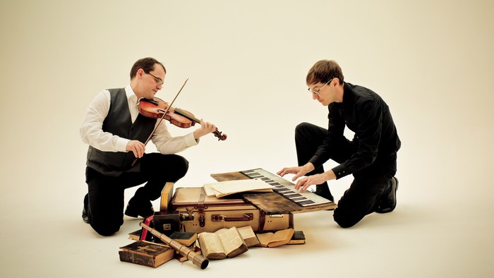 Zwei Männer spielen Geige und Klavier auf Koffern.
