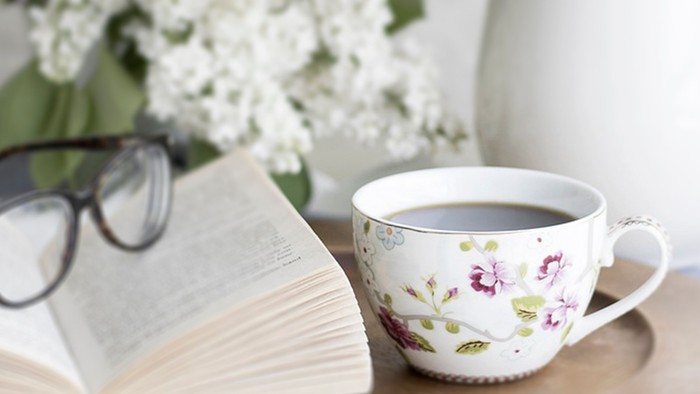 Ein Buch, eine Tasse Tee und eine Brille auf einem Tisch mit Blumen