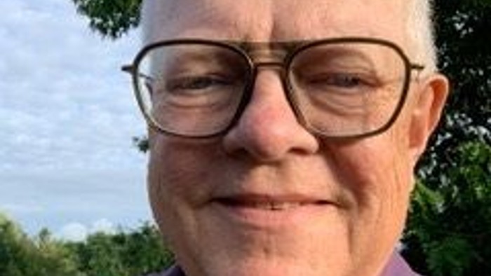 En smilende, glat-håret mand med briller og lilla polo-højt.