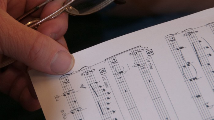 Hand hält eine Lupe über einem Notenblatt