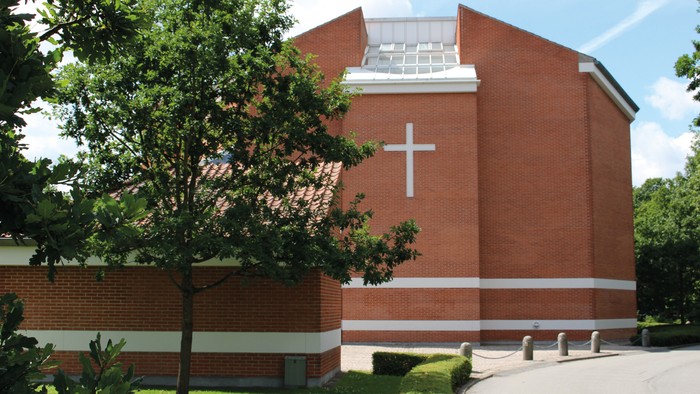 Et rødt murstenskirke med kors på fasaden og træ foran