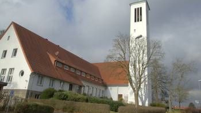 Ein weißes Gebäude mit rotem Dach und einem hohen Turm, umgeben von Bäumen und Büschen.