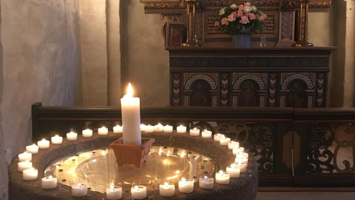 Døbefont med levende lys og et alter i baggrunden