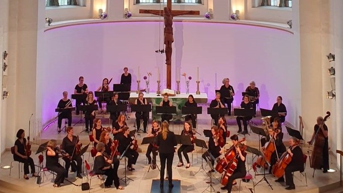 Ein Orchester spielt in einer Kirche vor einem großen Kreuz