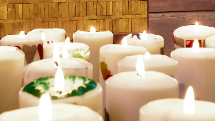 Viele brennende Kerzen vor goldener Kirchenwand mit Taube und Kreuz