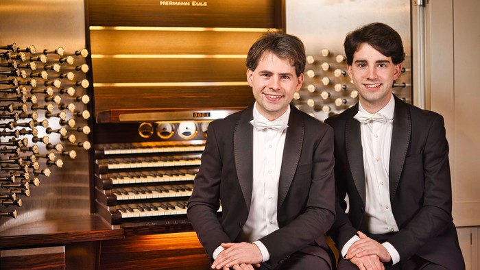 Zwei Männer in Anzügen sitzen vor einem großen Musikinstrument