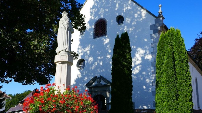 Weißes Kirchegebäude mit Turm und Statue davor