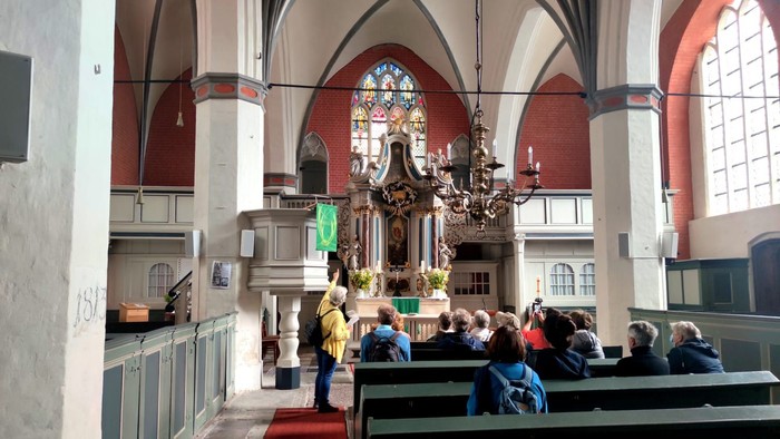 In der Kirche sitzen Menschen auf Bänken, vorne steht ein Altar.