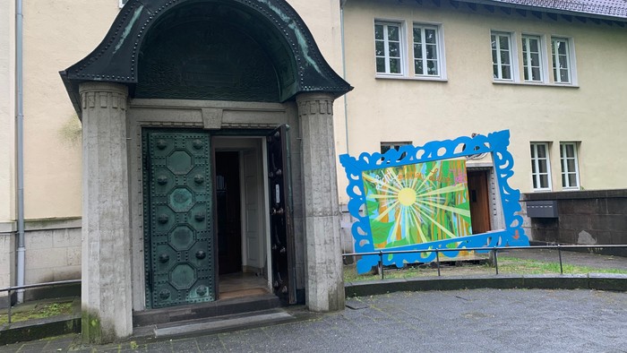 Ein dekorativer grüner Hauseingang mit einem bunten Wandgemälde und einem angrenzenden cremefarbenen Gebäude.