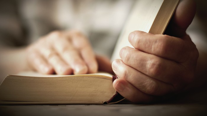 Hænder holder en åben bog.