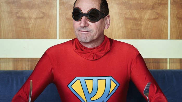 Mann im Superheldenkostüm isst am Tisch
