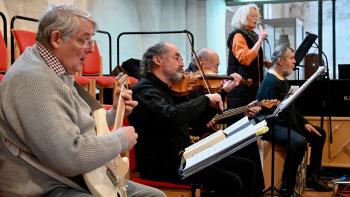 Eine Gruppe von älteren Musikern spielt verschiedene Instrumente in einem Raum
