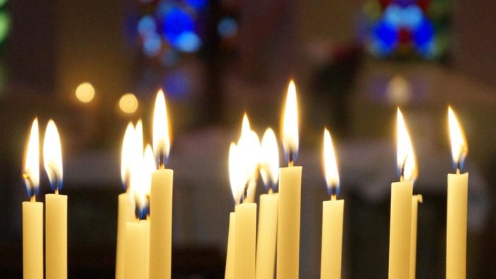 Mehrere brennende Kerzen vor Kirchenfenster