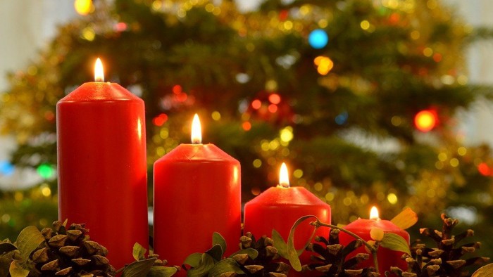 Fire røde lys på adventskranse foran juletree