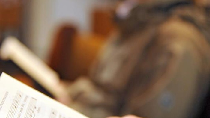 Eine Person hält ein Notenblatt, während sie Geige spielt.