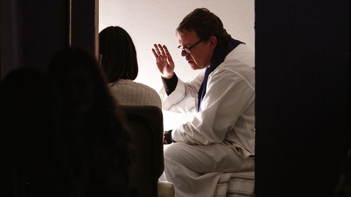 Ein Mann in weißem Anzug winkt auf einer Bühne.