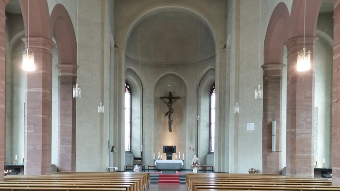Innenraum einer Kirche mit Holzbanken und Kreuz am Altar