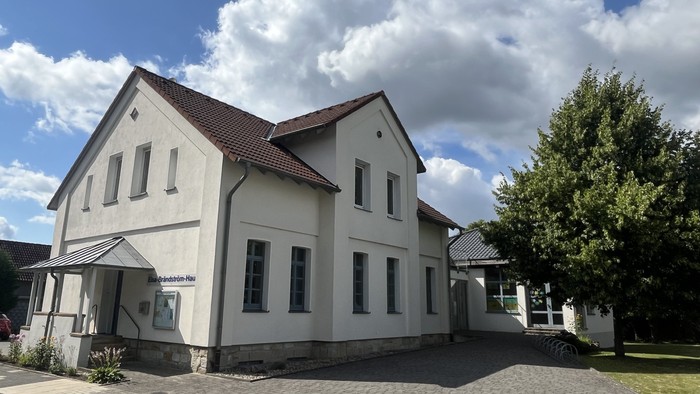 Das Bild zeigt das Laggenbecker Gemeindehaus, ein weiß verputztes Gebäude mit einem Anbau rechts.