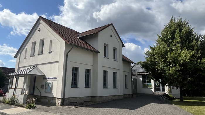 Das Bild zeigt das Laggenbecker Gemeindehaus, ein weiß verputztes Gebäude mit einem Anbau rechts.