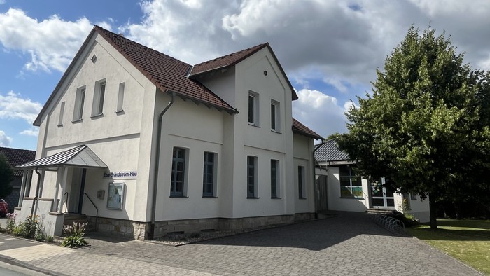 Das Bild zeigt das Laggenbecker Gemeindehaus, ein weiß verputztes Gebäude mit einem Anbau rechts.