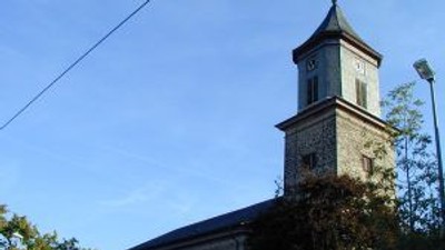 Kirche mit hohem Glockenturm unter klarem blauem Himmel.