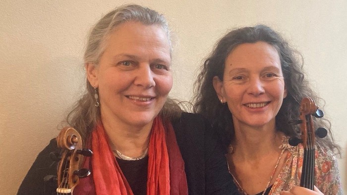 Zwei Frauen, die lächeln, während sie ihre Violinen halten und posieren.