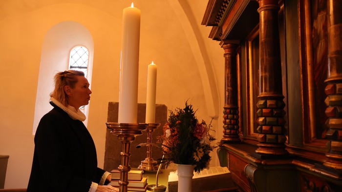 Kvinde i kirke, der kigger på lys og blomster.