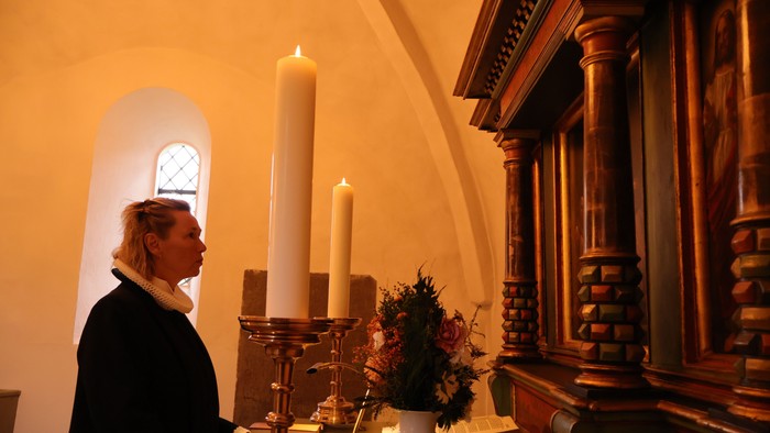Kvinde i kirke, der kigger på lys og blomster.