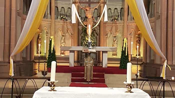 Eleganter Kirchenaltar, geschmückt mit Kerzen, religiösen Symbolen und verziert mit dekorativen Stoffen.