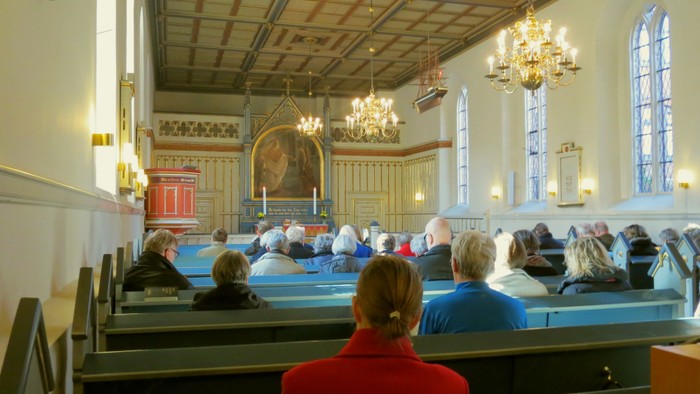 En kirke med folk på bænkene og et alter med lys.