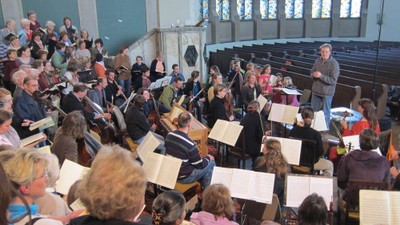 Ein Orchester probt in einem großen Saal unter der Leitung eines Dirigenten.