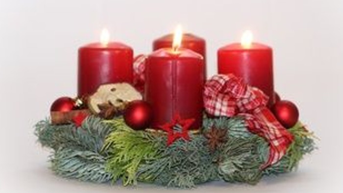 Drei brennende rote Kerzen auf grünem Kranz mit Weihnachtsdekoration
