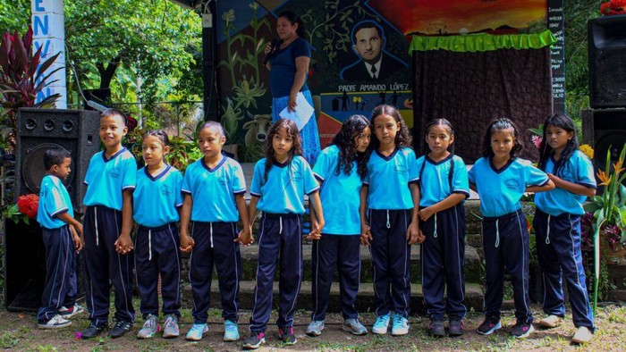 Eine Gruppe von Kindern in blauen Hemden und dunklen Hosen posiert vor einem bunten Wandgemälde.