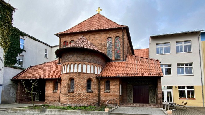 Das Bild zeigt eine rote Backsteinkirche mit spitzem Dach und einem kleinen Turm.