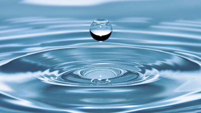 Ein Wassertröpfchen trifft auf Wasseroberfläche und erzeugt Wellenkreise