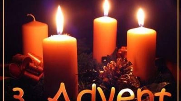 Tre lysende adventstænder omgivet af nåle og frugter