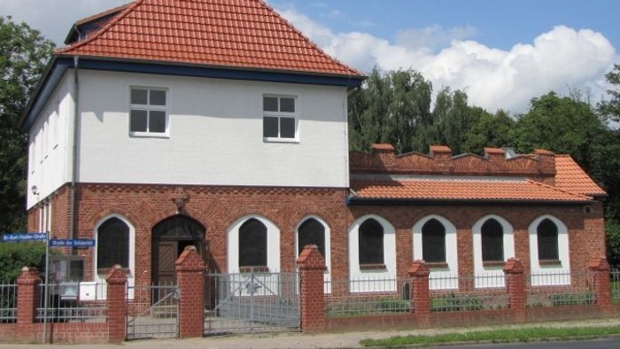 Weißes Gebäude mit rotem Dach und Turm, umgeben von einem Zaun