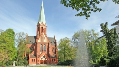 Ein rotes Kirche mit hohem Turm und ein Brunnen im Vordergrund