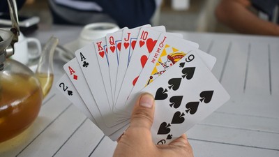 Eine Hand hält einen Fächer ausspielkarten auf einem Tisch mit Teekanne