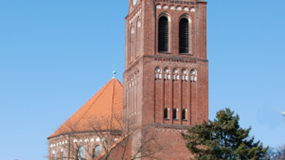 Große rote Backsteinkirche mit hohem Turm und spitzem Dach.