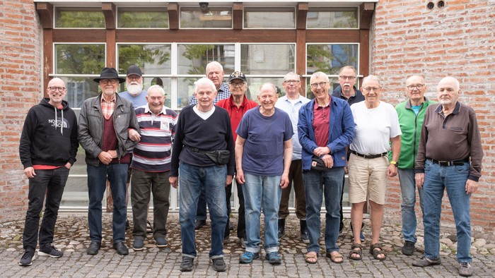 En gruppe af mænd står sammen udenfor et murstenshus.