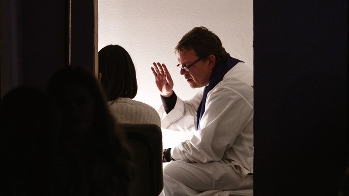 Ein Mann in weißem Anzug winkt auf einer Bühne.