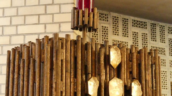 Ein hölzerner Kronleuchter mit goldenen Akzenten vor einer weißen Ziegelwand.