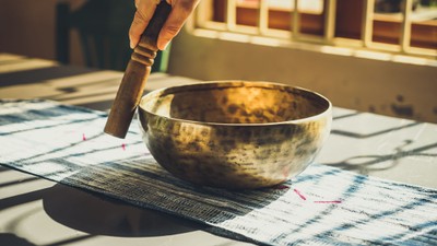 Eine Hand schlägt mit einem Hammer auf eine Metallschale, die auf einem blauen und weißen Tuch liegt.