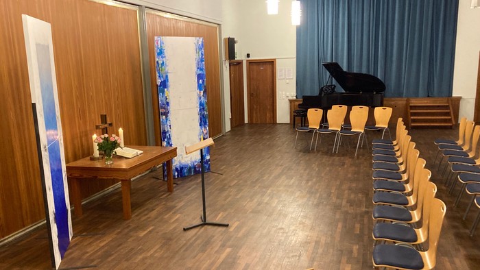 Ein geräumiger Raum mit Holzbestuhlung für eine Veranstaltung, ausgestattet mit einem dekorierten Altar und einer Bühnenrückwand.