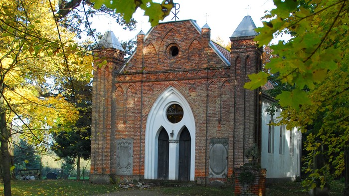 Ein altes Backsteingebäude mit spitzen Bögen, umgeben von Herbstlaub und Bäumen