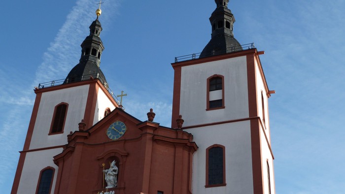 Elegante Kirche mit Zwillingstürmen, Ziffernblatt und verzierter Fassade vor einem klaren blauen Himmel.